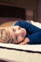 Happy kid lying down on bed and looking at camera. photo