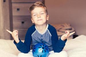 Small boy in lotus pose meditating with eyes closed in bedroom. photo