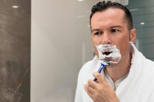 hombre adulto medio afeitándose en el baño. foto