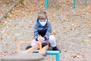 Pensive boy with protective face mask relaxing at the playground. photo