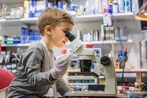 pequeño estudiante examinando la placa de circuito a través del microscopio. foto