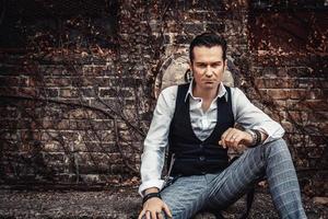 Portrait of serious retro-styled man relaxing against brick wall. photo