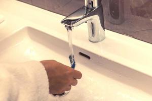 Close-up of man rinsing razor while shaving in the bathroom. photo