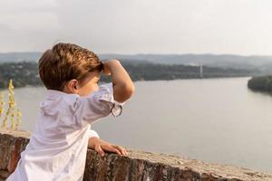 niño pequeño en la orilla del río mirando la vista al atardecer foto