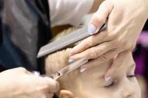 Close up of hairdresser cutting boy's hair at the salon. photo