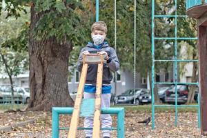 Pensive boy wearing face mask while playing alone at the playground. photo