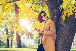 Happy fashionable woman using mobile phone in park. photo