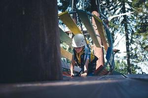 niño pequeño arrastrándose a través de obstáculos durante el curso de cuerdas en la naturaleza. foto