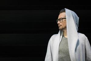 Profile view of man in hooded jacket against black wall. photo