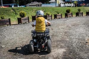 Rear view of boy learning to drive quad bike on dirt road. photo