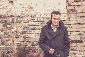 Portrait of serious man in coat next to brick wall. photo