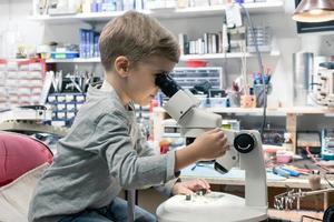 Little boy examining computer part while looking through the microscope. photo