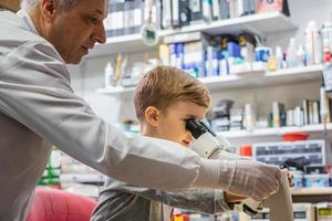 Teacher and little boy examining something through the microscope in laboratory. photo