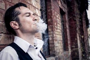 Thoughtful man smoking while leaning on brick wall. photo