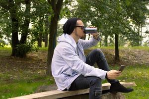 Mid adult man using mobile phone while drinking takeaway coffee in nature. photo