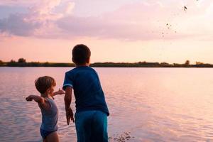 chicos juguetones tirando arena en el agua al atardecer. foto