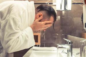 Man in bathrobe washing his face in the morning. photo