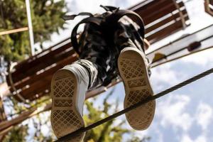 Below view of boy crossing over hanging rope on canopy tour in nature. photo