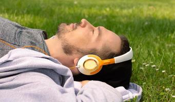 Profile view of man man relaxing on grass while listening music over headphones. photo
