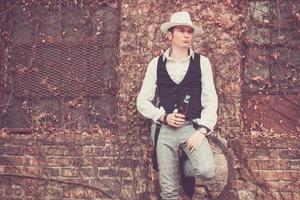 hombre de estilo fedora con botella de cerveza contra la pared. foto