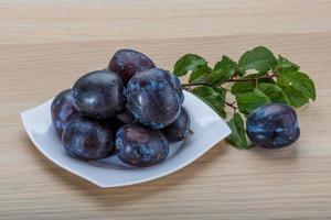 ciruelas frescas en el plato y fondo de madera foto