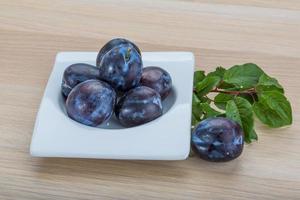 Fresh plums in a bowl on wooden background photo