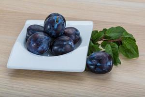 Fresh plums in a bowl on wooden background photo