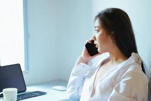 The new normal. A businesswoman is using her phone and computer to work for a company. over the Internet on your desk at home. photo