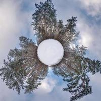 Winter tiny planet in snow covered forest in blue sky. transformation of spherical panorama 360 degrees. Spherical abstract aerial view in forest. Curvature of space. photo