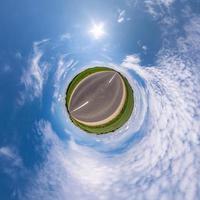 green tiny planet in blue sky with sun and beautiful clouds. Transformation of spherical panorama 360 degrees. Spherical abstract aerial view. Curvature of space. photo