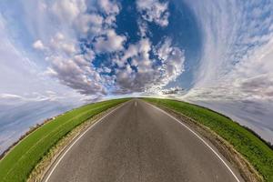 hemisphere of the planet on an asphalt road stretching beyond the horizon with blue sky and beautiful clouds. Spherical abstract aerial view. Curvature of space. photo
