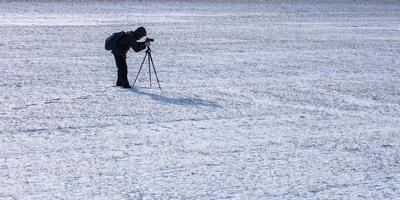 photographer with a tripod in snowy field takes pictures of landscape, footprints in snow photo