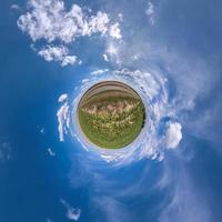 green tiny planet in blue sky with beautiful clouds. Transformation of spherical panorama 360 degrees. Spherical abstract aerial view. Curvature of space. photo