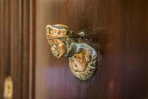 Old wooden doors with rings and old-fashioned vintage steel knocker handle shaped like a woman's head close up in Italy. photo