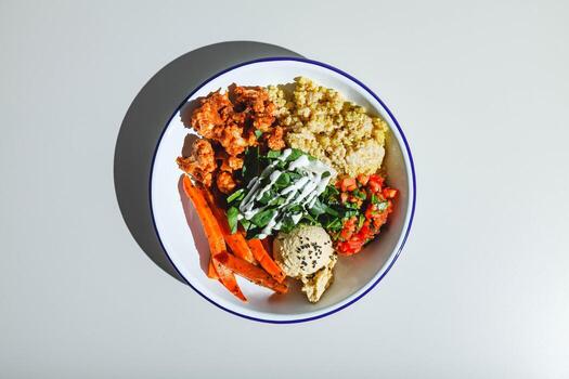 tazón vegetariano con quinoa, zanahorias, coliflor en salsa, espinacas, tomates y hummus. luz dura, sombra profunda foto