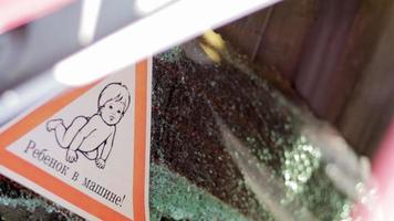 avvertimento cartello di bambini dentro un' auto dopo un incidente con rotto bicchiere. traduzione bambino nel il macchina. un' avvicinamento di un' bambino su un' etichetta, su il posteriore finestra di un' macchina. video