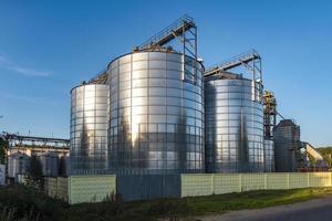 ascensor de granero moderno con silos de plata en la planta de procesamiento y fabricación de productos agrícolas para el procesamiento, secado, limpieza y almacenamiento de productos agrícolas, harina, cereales y granos. foto