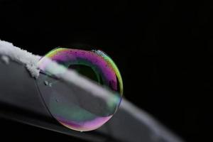 A shimmering soap bubble on a metal arch against a dark background in winter photo