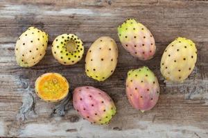 Several ripe prickly pears lie on a board of old weathered wood. A fruit is cut open. photo