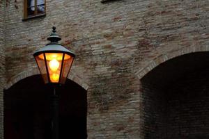 a glowing lantern stands in front of old and historic brick walls at dusk in the evening photo
