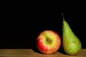 una manzana y una pera yacen una al lado de la otra sobre una mesa contra un fondo oscuro foto