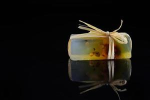 A piece of homemade soap is wrapped in raffia and reflected against a dark background photo