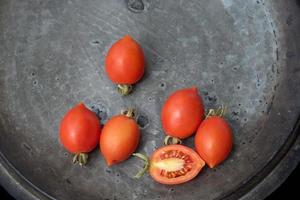 On an old, gray copper plate lies a group of small red tomatoes, photographed from above. The tomatoes are pointed at the front and come from Sicily. There is space for text. photo