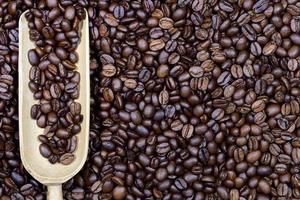 Close up, texture and background of roasted fresh coffee beans with a small wooden scoop in it photo