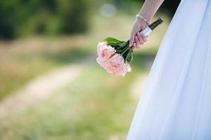 novia con un vestido blanco con un ramo de novia de rosas blancas y rosas en el parque foto