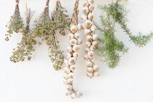 Various herbs such as oregano and rosemary hang next to garlic to dry on the white rustic wall photo