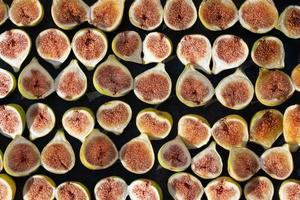 Many green, freshly cut figs lie next to each other in front of a dark background. They are photographed from above. photo