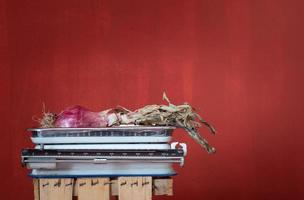 An old kitchen scale stands against a red background with space for text. There is a red onion on the scales. photo