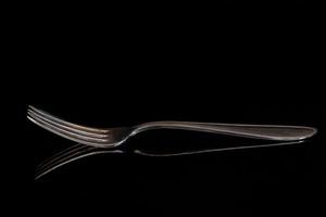 Close-up of an empty old fork with long tines reflected against a dark background.
