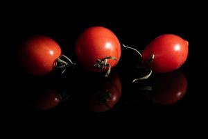 Close-up of three red ripe tomatoes lying side by side against a dark surface. The tomatoes are reflected on the background. photo